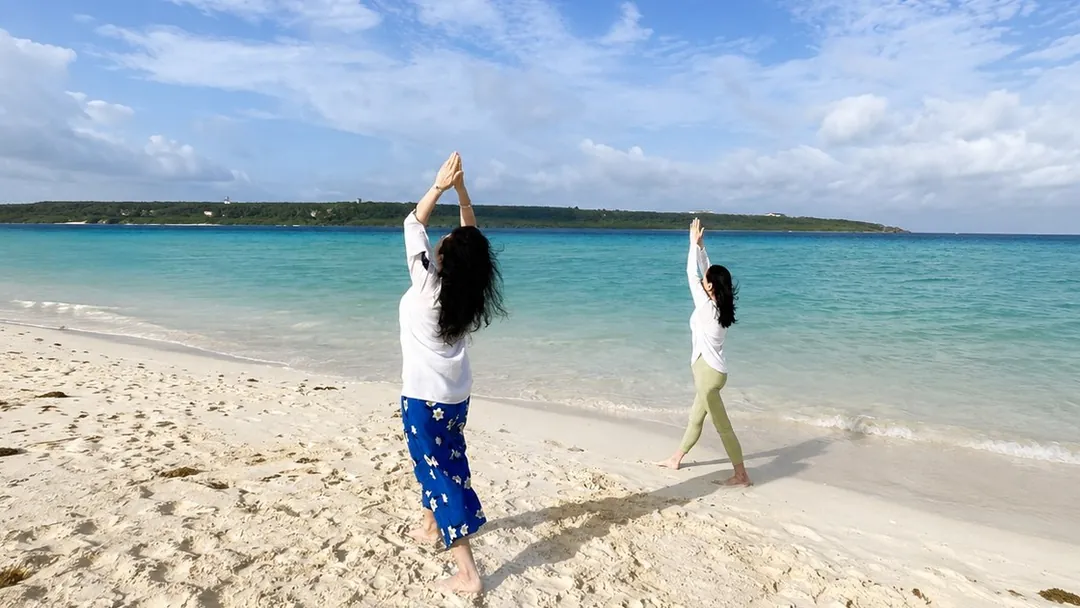 海辺で両手を頭上に上げ、深い呼吸を行う参加者